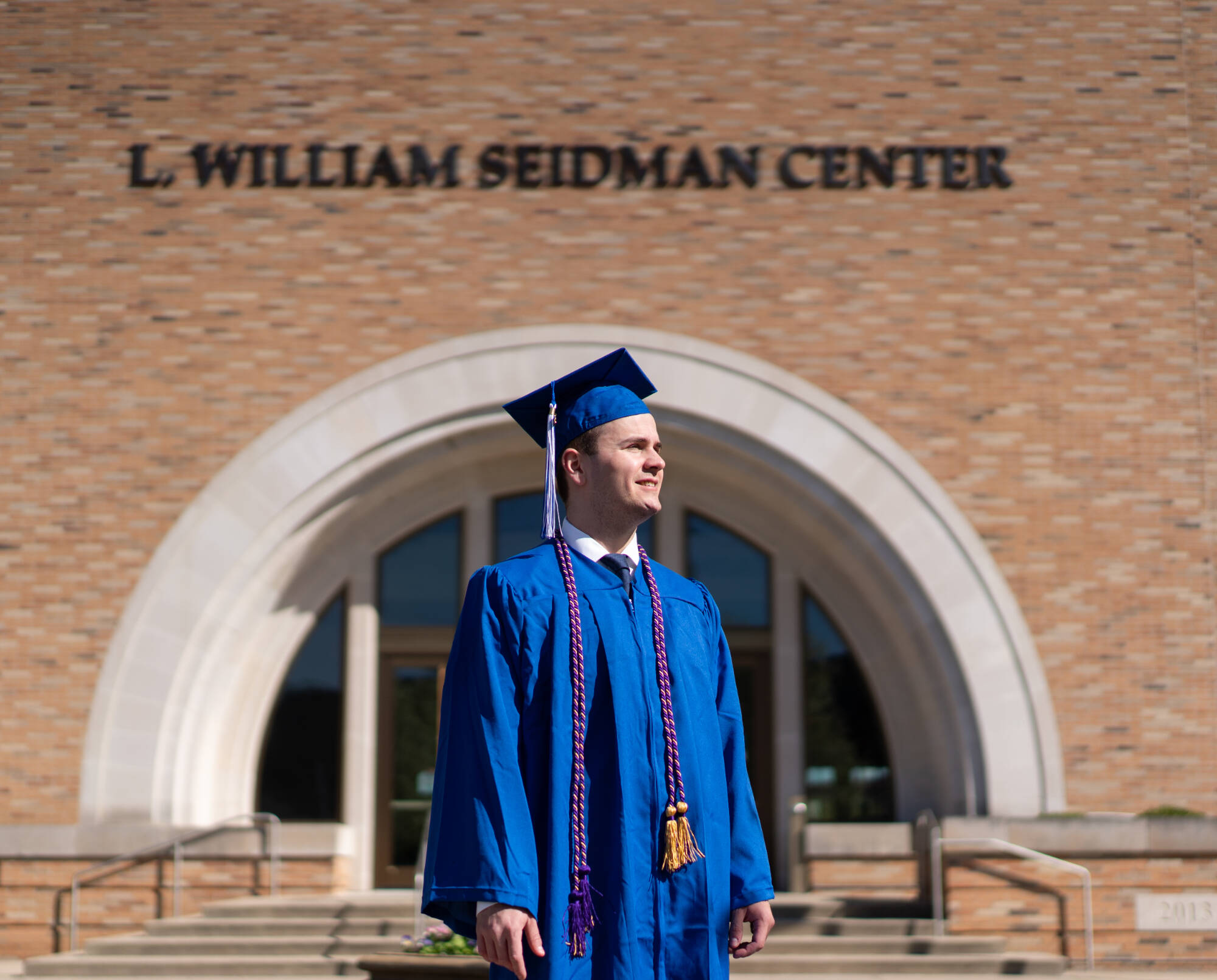 Student standing in front of Seidman building in a cap and gown